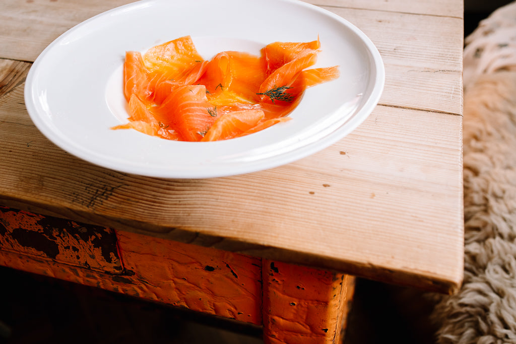 Smoked salmon and dill in a white bowl on a wooden table with orange legs.