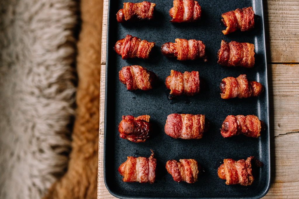 streaky bacon pigs in blankets on a black serving plate