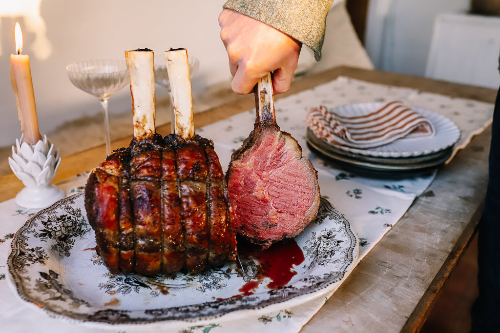 Bone in Christmas rib roast, cooked with hand holding one bone showing it cooked medium rare inside.