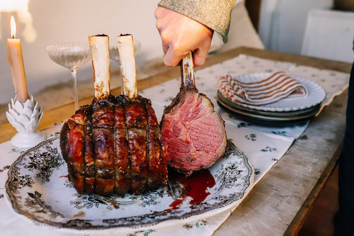 Bone in Christmas rib roast, cooked with hand holding one bone showing it cooked medium rare inside.
