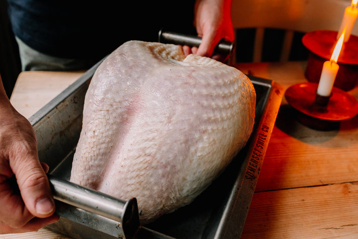 Raw turkey in a roasting tray beside some candles